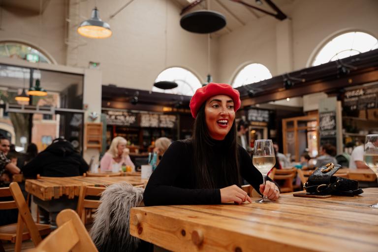 Smiling woman with red beret and glass of white wine in Altrincham Market