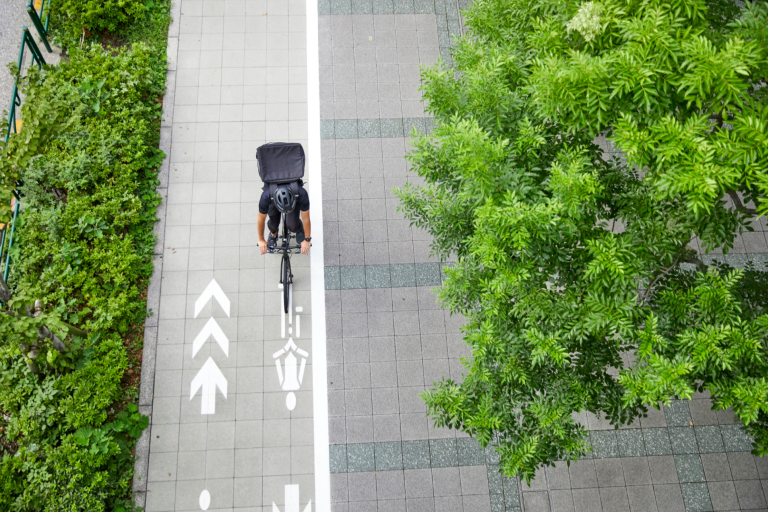 Cyclist with food delivery on cycle lane with bush and tree on either side