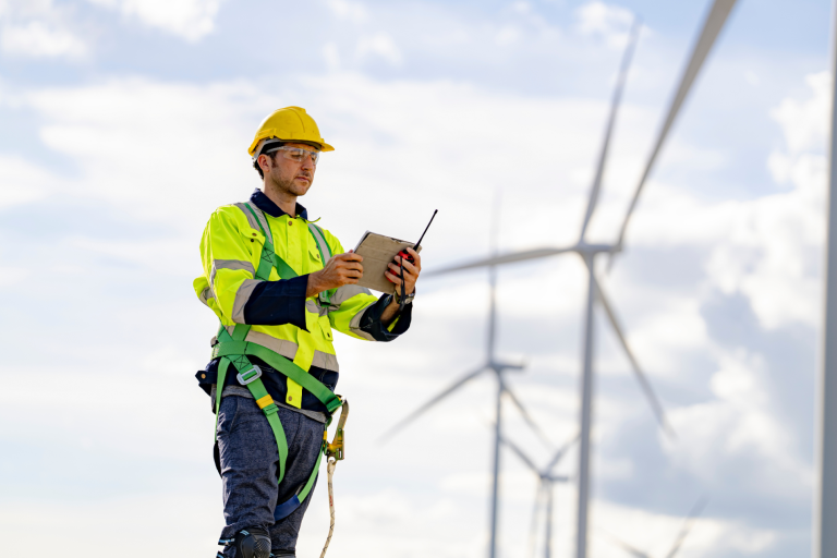 Worker in high vis and hat looking at phone on top of a wind turbine